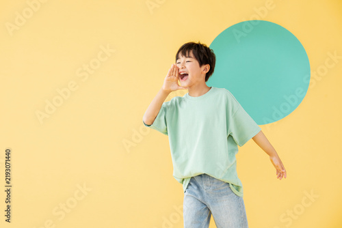 Cheerful Boy Shouting with Hand Near Mouth on Yellow Background