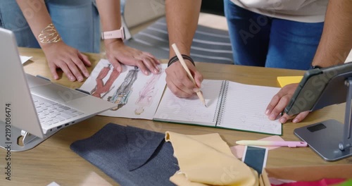 Two designers leaning forward, sketching in spiral notebook and using swatches, noting measurements