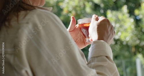 Camera panning is revealing hands cradling tea cup and are lifting toward mouth, sipping on balcony
