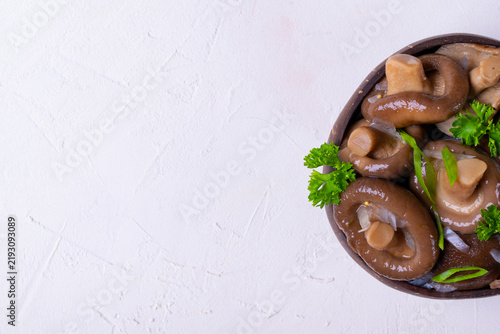 Pickled milk mushrooms with onion and spices topped with parsley in wooden bowl on white background. Russian cuisine appetizer. Copy space