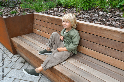 Little boy sitting on a wooden bench in a landscaped urban garden