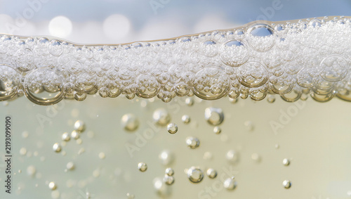 Macro close up of sparkling champagne bubbles and foam at the surface of a golden drink, celebration beverage concept with wide copy space for text
