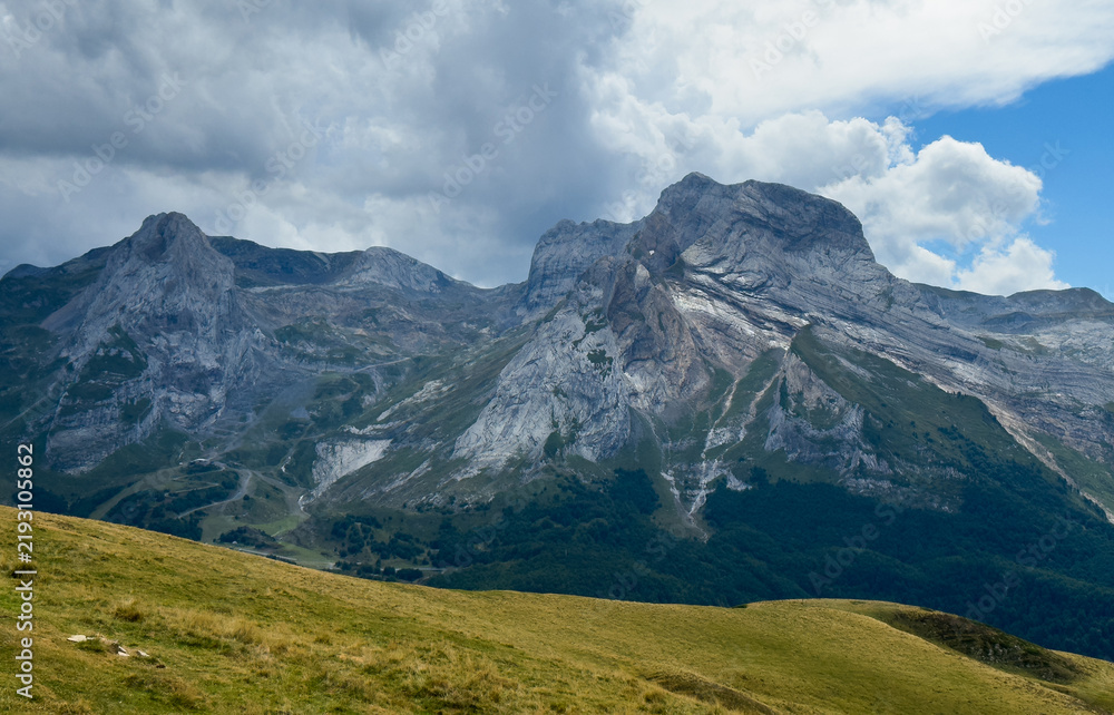 Obraz premium serene mountain peak standing tall in rugged landscape with grassy foreground and cloudy sky from a lower vantage point looking up at the majestic nature photography destination.