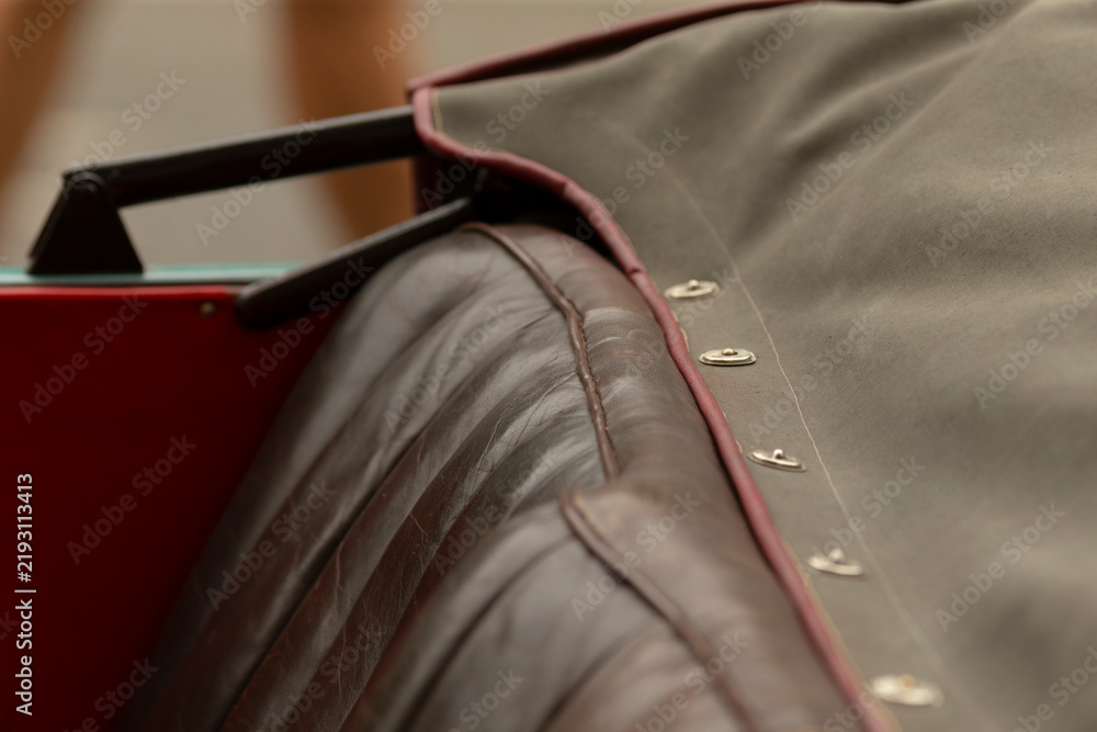 Obraz premium Close-up view of a brown quilted leather car seat partially covered by an olive canvas tonneau cover secured with brass snap fasteners. Visible folded edge