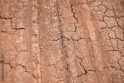 Fotografía Cracked dry earth texture of a dusty rural road with tire track imprints under bright sunlight