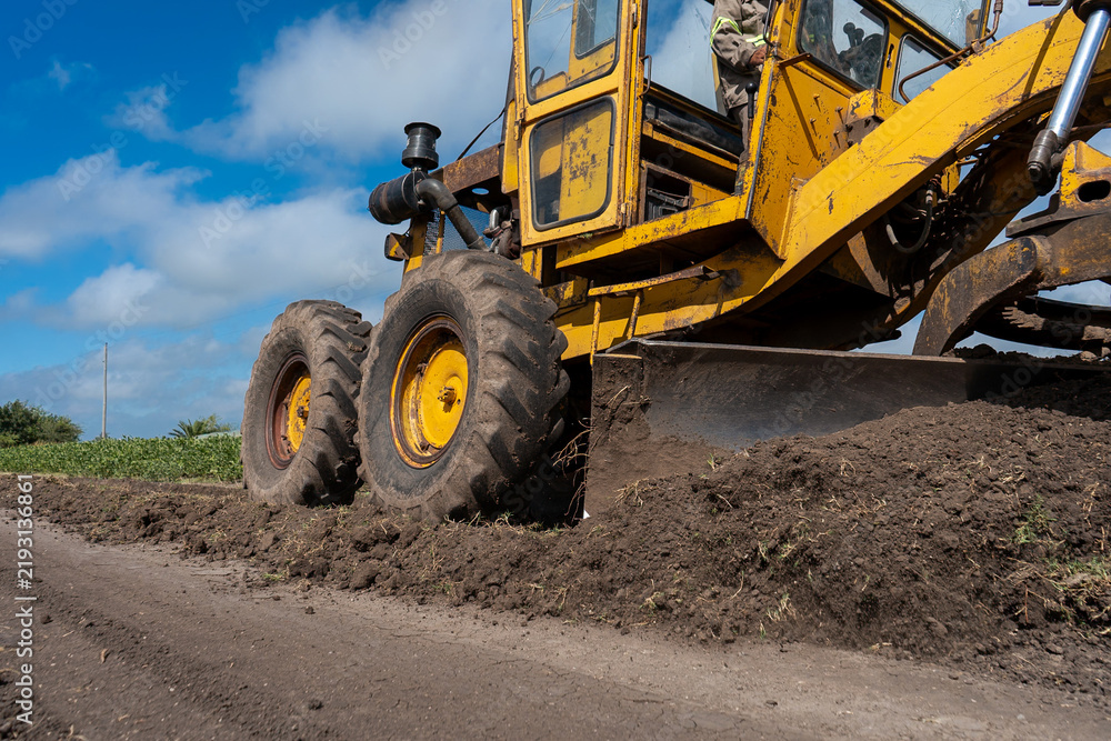 Fototapeta premium Yellow motor grader pushing and leveling soil on a rural dirt road