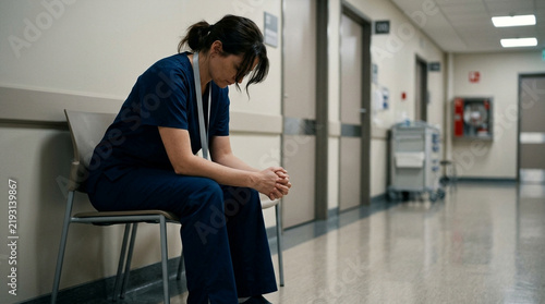 Exhausted medical professional sitting in a hospital corridor looking down, feeling overwhelmed