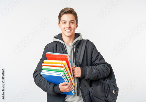 Happy student boy holding colorful books and a backpack