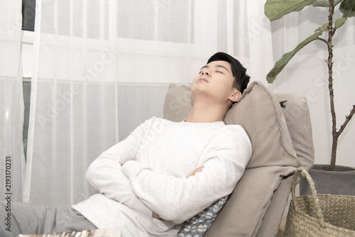 Картината върху платно Young man relaxing with eyes closed and arms crossed on a sofa at home