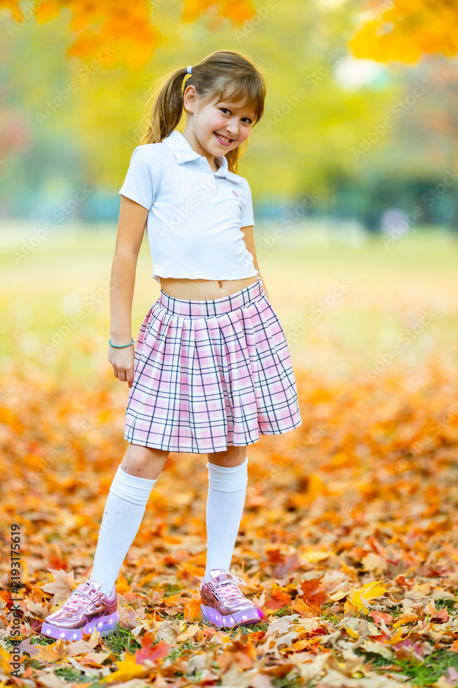 Obraz premium Autumn girl wears a sequin jacket. Autumn child carries maple leaves. Colorful autumn foliage blurs behind. Happy autumn lifestyle portrait.