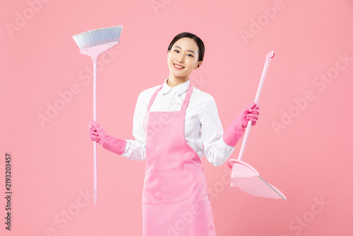 Fotografía Smiling woman in pink apron holding cleaning tools for housekeeping service