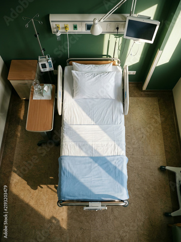 Hospital bed with white linens and a blue blanket in a green room in soft daylight
