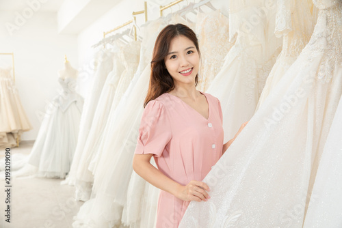 Happy Asian woman choosing a white wedding dress in a bridal shop