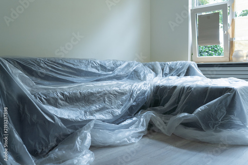 Furniture covered with protective film before room renovation, wall painting, and ceiling work to prevent dust and paint damage. 
