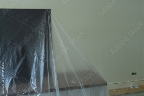 Furniture covered with protective film before room renovation, wall painting, and ceiling work to prevent dust and paint damage. 