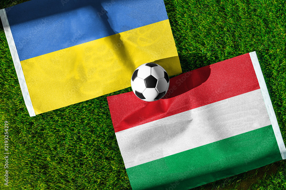 Fototapeta premium Ukraine vs. Hungary football match. National flags on green grass with soccer ball in the middle. Football background for international match.