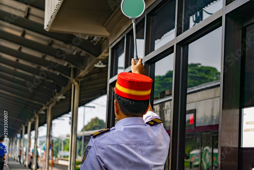 Fotografie A station master complete with his uniform and red hat is holding up the green s