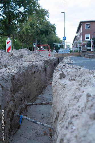 Workers have dug trenches for utility installation, with pedestrian zones organized using small bridges across the ditches.