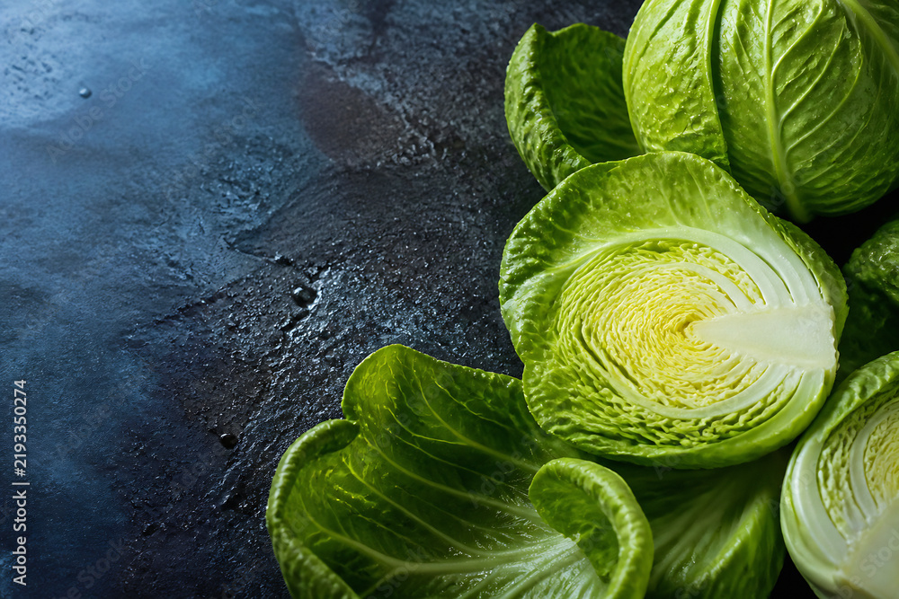 Fototapeta premium Bright green cabbage heads are arranged on a dark, textured surface.