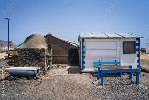 Картината върху платно A traditional stone oven and repurposed bathtub sit beside a blue-trimmed shack in the small settlement of El Jablito, Fuerteventura, Canary Islands, Spain