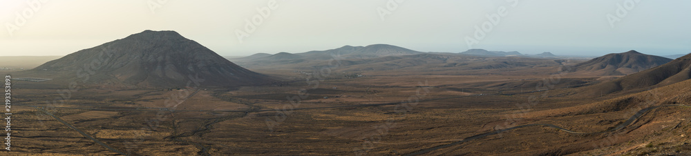 Naklejka premium A panoramic view from Mirador de Vallebron shows arid plains and Montana Tindaya rising on the right, with distant mountains along the horizon, Fuerteventura, Canary Islands, Spain.