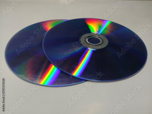 фотографія Two blank compact discs showing colorful rainbow light reflections on a white ba