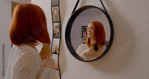 Bild auf Leinwand Red haired woman performing morning hair care routine, brushing locks while exam