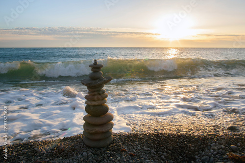 Photography Zen stone cairn on a pebble beach at sunset, with waves breaking in the background