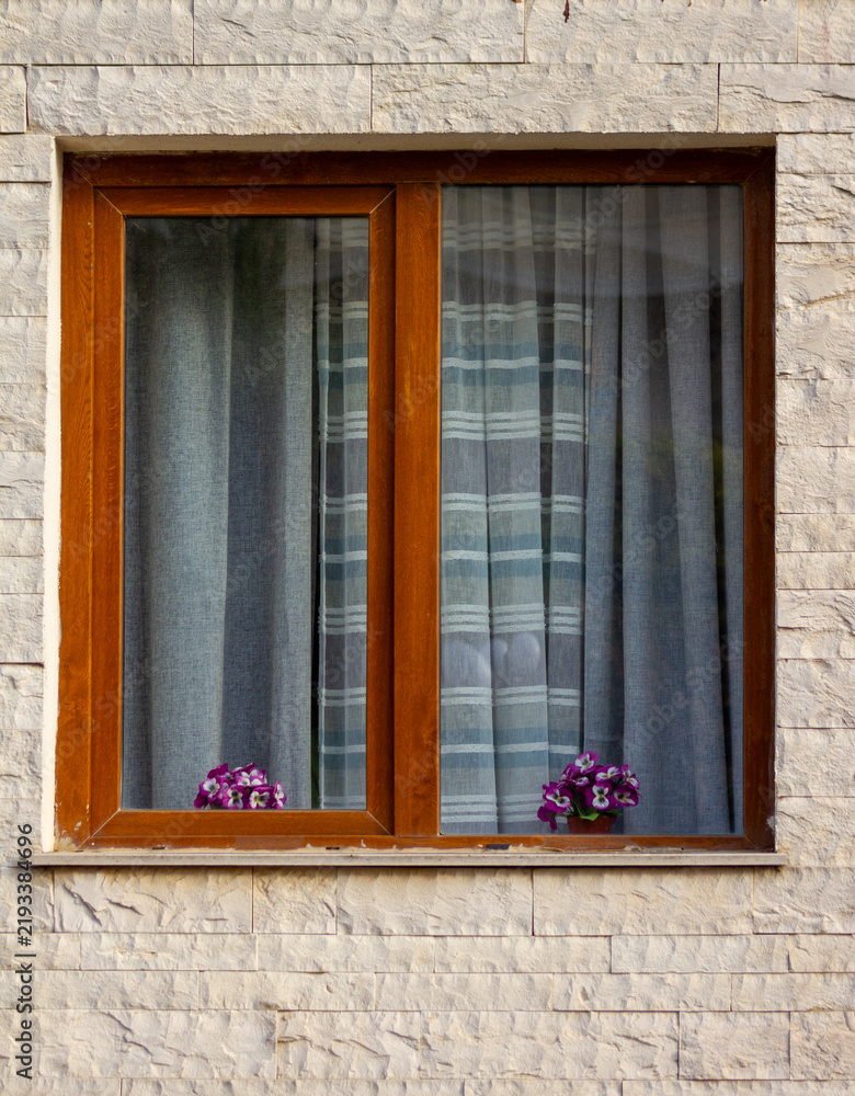 Obraz premium Wooden window frame with sheer curtains and purple flowers on windowsill