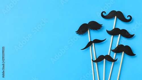 Collection of black paper mustaches on sticks against a bright blue background