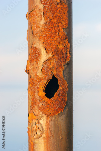 Obraz na plátně Close-up of a heavily rusted metal pole with peeling corrosion and a large hole, isolated against a bright sky, showing weathering, decay, and industrial deterioration