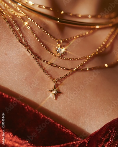 Close-up fashion detail of layered gold necklaces featuring a star pendant, sparkling accents, and a rich red velvet garment, ideal for festive occasions and holiday celebrations