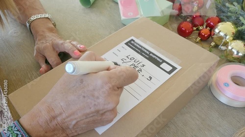 Elderly woman writing shipping address on christmas package