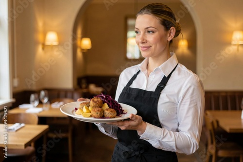 Waitress holding plate of Frikadeller, pork meatballs with onions, breadcrumbs, spices in cozy restaurant with warm lighting, wooden tables. Concept of hospitality and comfort in dining.