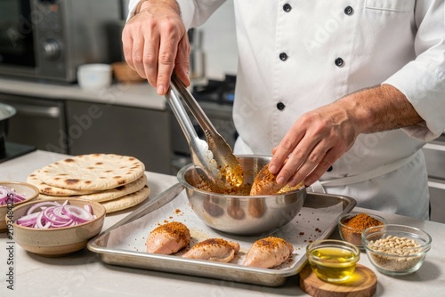 Chef in modern kitchen preparing Musakhan, traditional dish with flatbread topped with chicken, onions, sumac, and pine nuts. Concept of culinary artistry and spice blending.