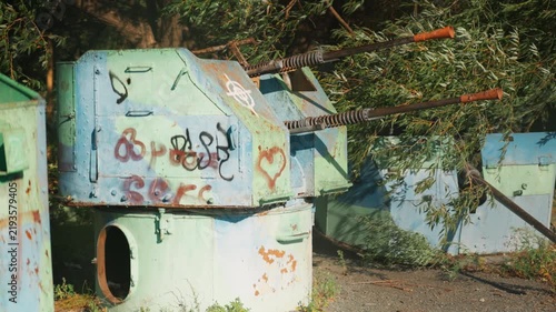 
Obsolete, abandoned, and rusty combat guns with a heart painted on the body stand amidst the natural landscape. A graveyard of weaponry. An echo of war.