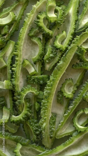 Close-up of exotic fresh bitter melon. Tight composition of densely packed bitter gourd halves with the white core removed, topped with small sliced half-moons. Vertical video.