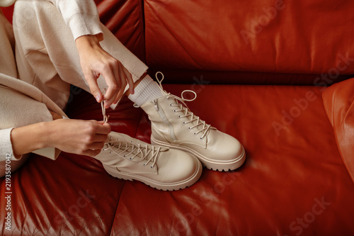 Close up shot of woman`s hands tying laces of white leather lace-up ankle boots with track sole. Autumn, winter fashion trend. Copy, empty space for text
