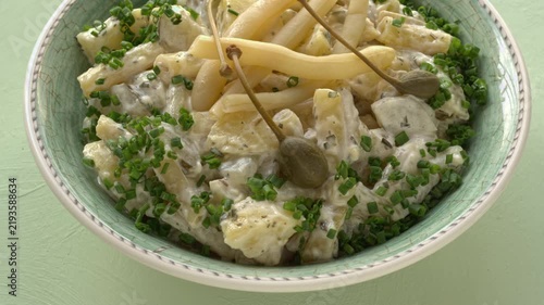 Potato salad with a twist: replace pickled cucumbers with fermented yellow snap beans and top with caper berries. Pastel green background, table spin.