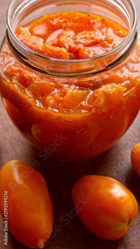 Tomato puree made from Orange Banana heritage tomatoes, packed in a glass barrel jar, set against a wooden background surrounded by fresh, whole Orange Banana tomatoes. Table spin. Vertical video.
