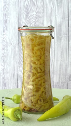 Jar of Asian-style pickled Hungarian Hot Wax chilies rotating in a static, subtle tilt view. Some whole chilies of the same variety near the jar. Vertical video.