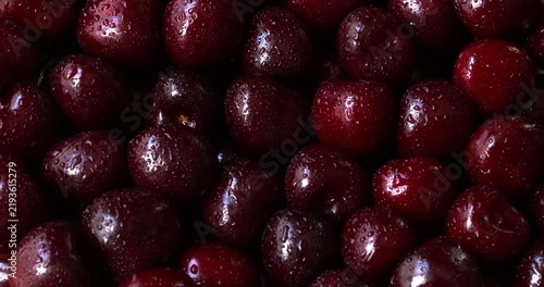 Sweet cherries with water droplets, full-frame background texture with light reflections. Close-up of ripe, organic fruits without stems, slowly rotating in natural light. 