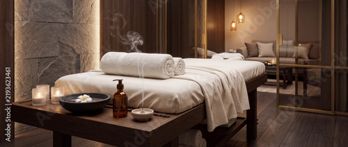 Massage table in luxury spa room prepared with fresh white towels, smoking incense, scented oil, and glowing candles for relaxing wellness therapy and body care treatment