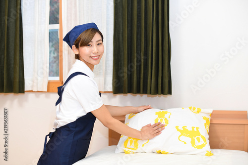 A smiling Asian female housekeeper making the bed.
