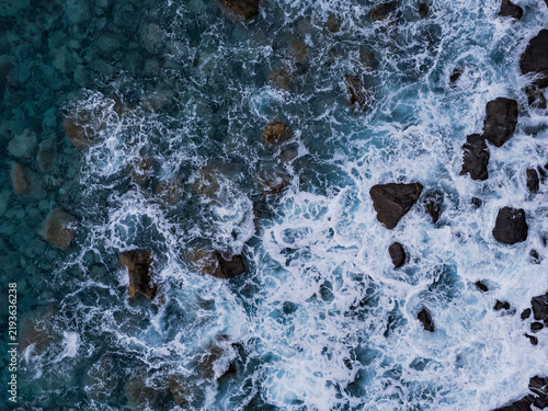 Clear ocean water with waves breaking over coastal rocks. Aerial top view of Atlantic shoreline with foam and stone texture