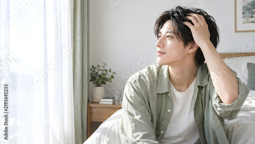髪をかき上げながら窓辺を見つめる男性 柔らかな自然光と透明感のある肌が映える自宅の美容スキンケア広告向けコピースペース