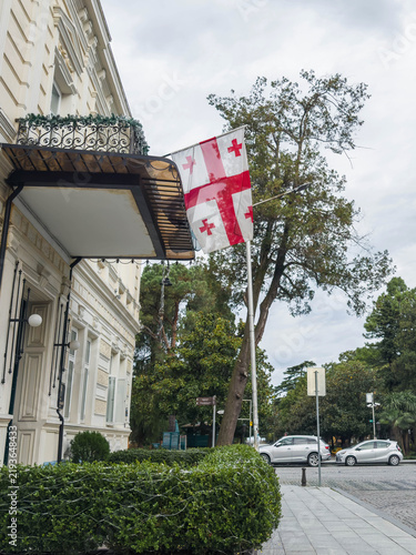 Cuadro en lienzo Georgian flag displayed beside ornate historic building, manicured greenery, tre