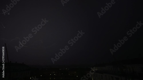 Multiple lightning branches illuminate black night sky over quiet neighborhood
