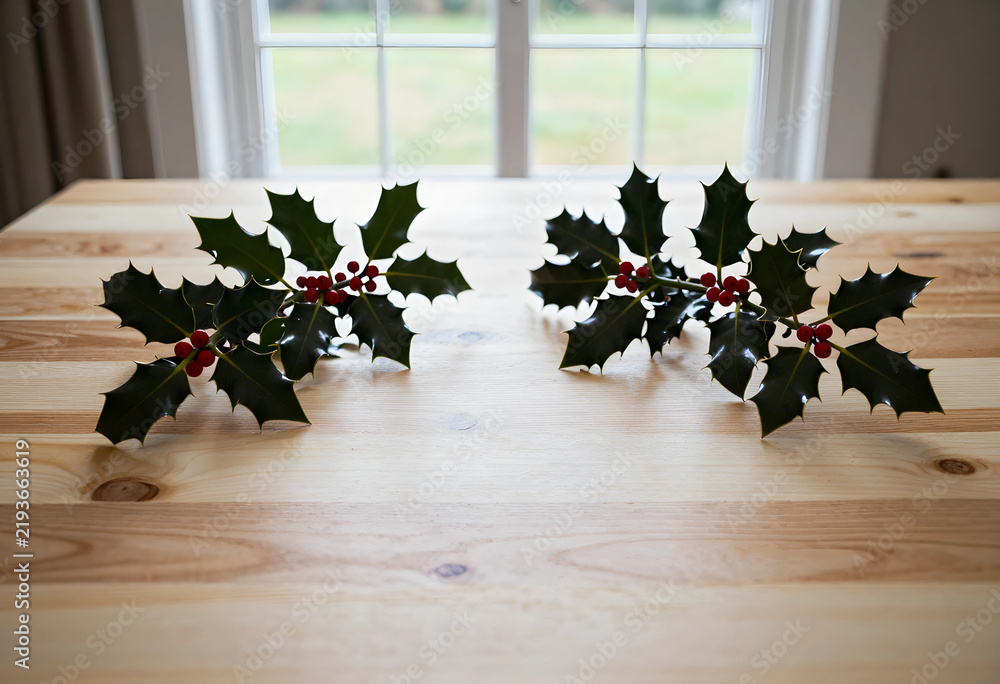 Obraz premium Christmas holiday decoration, holly branches with red berries on a natural wooden table for festive seasonal home interior and winter celebration