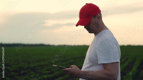 Agriculture, Field survey with technology, Modern day farmer s routine, Red cap farmer with phone, Soil inspection with digital tools, Farm tech trends, Connected devices in agriculture, Man planning